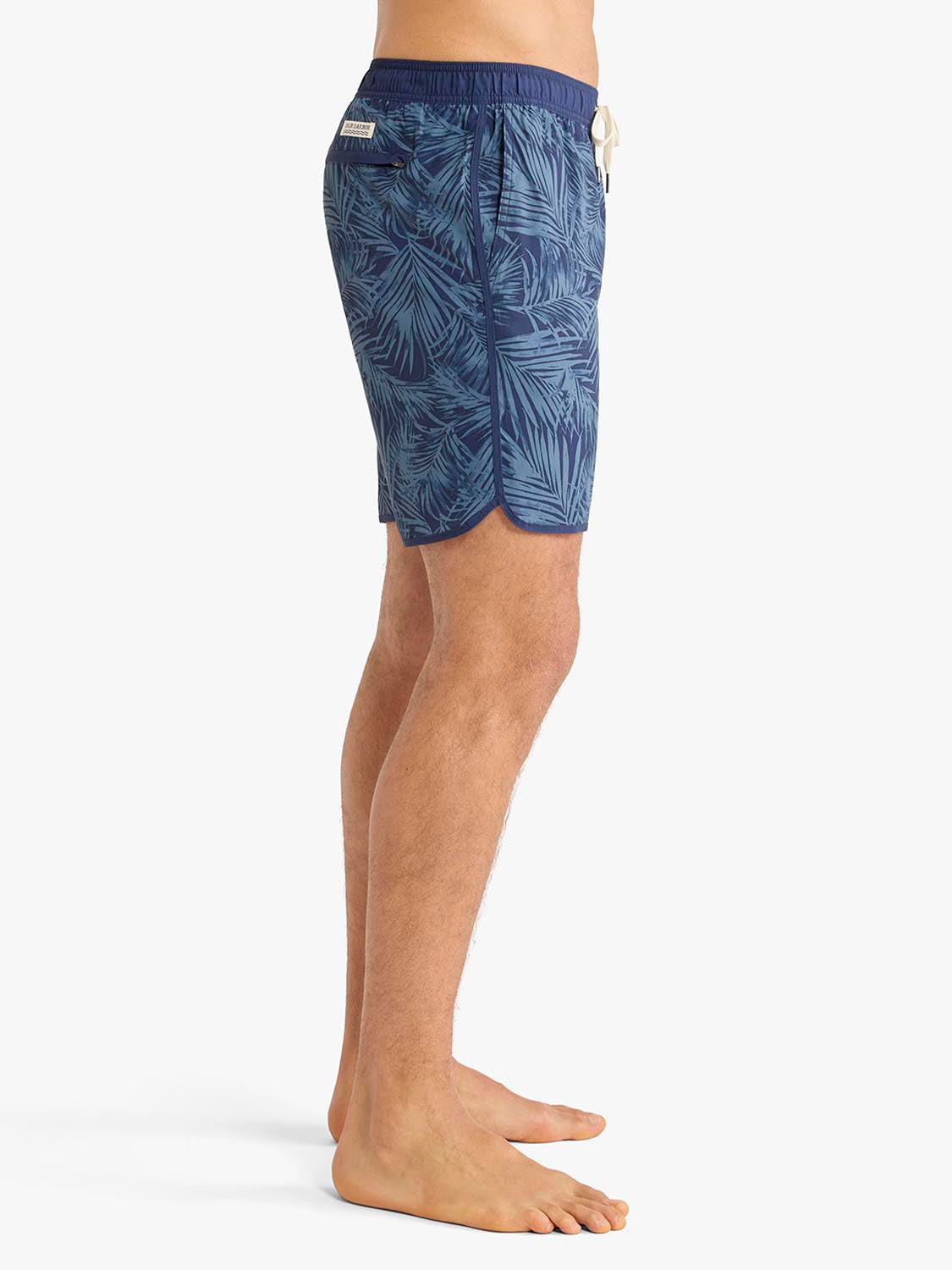 Man wearing navy blue swim trunks with leaf pattern print and drawstring waistband.