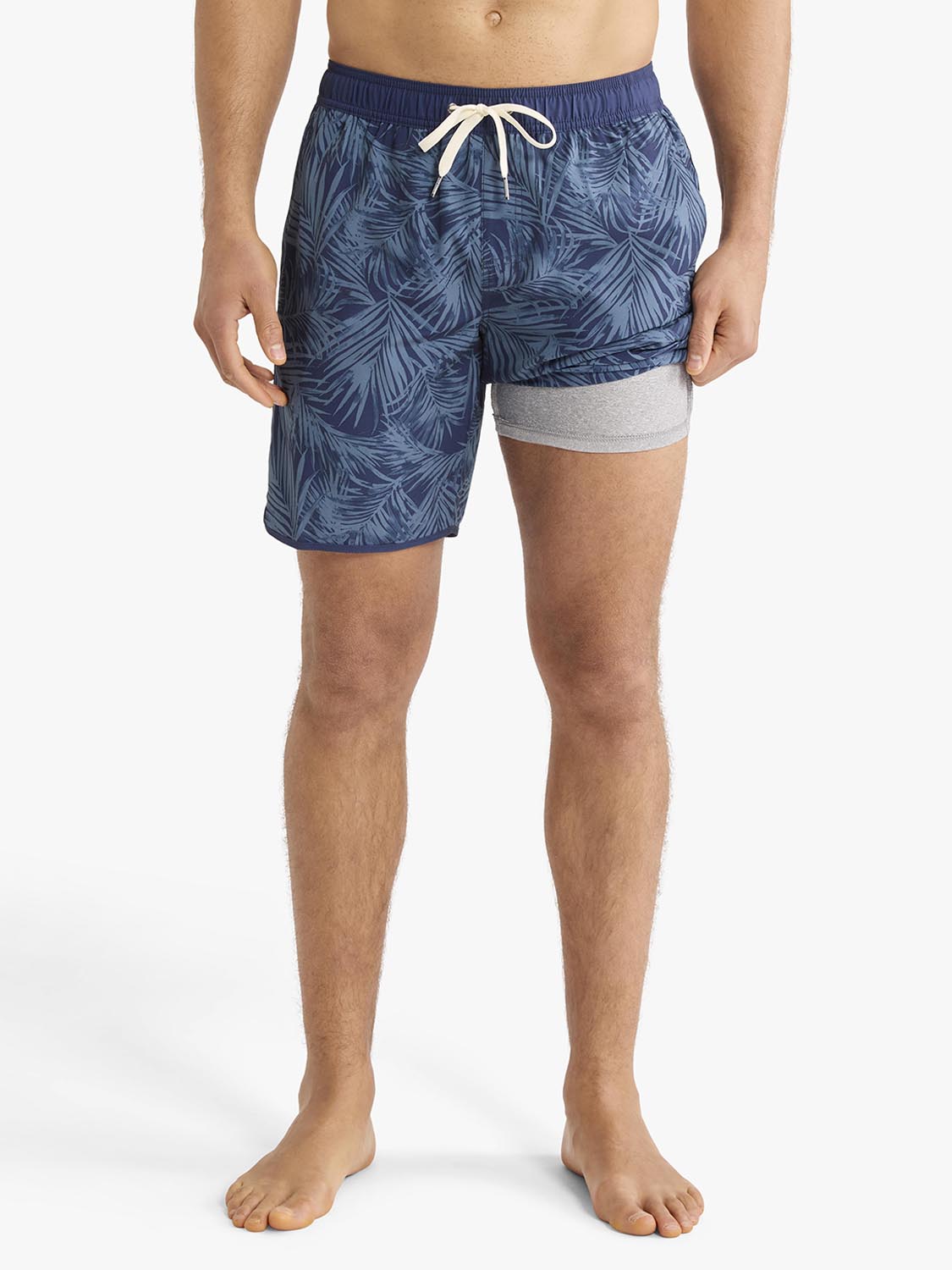 Man wearing navy swim trunks with blue leaf pattern and grey inset shorts.