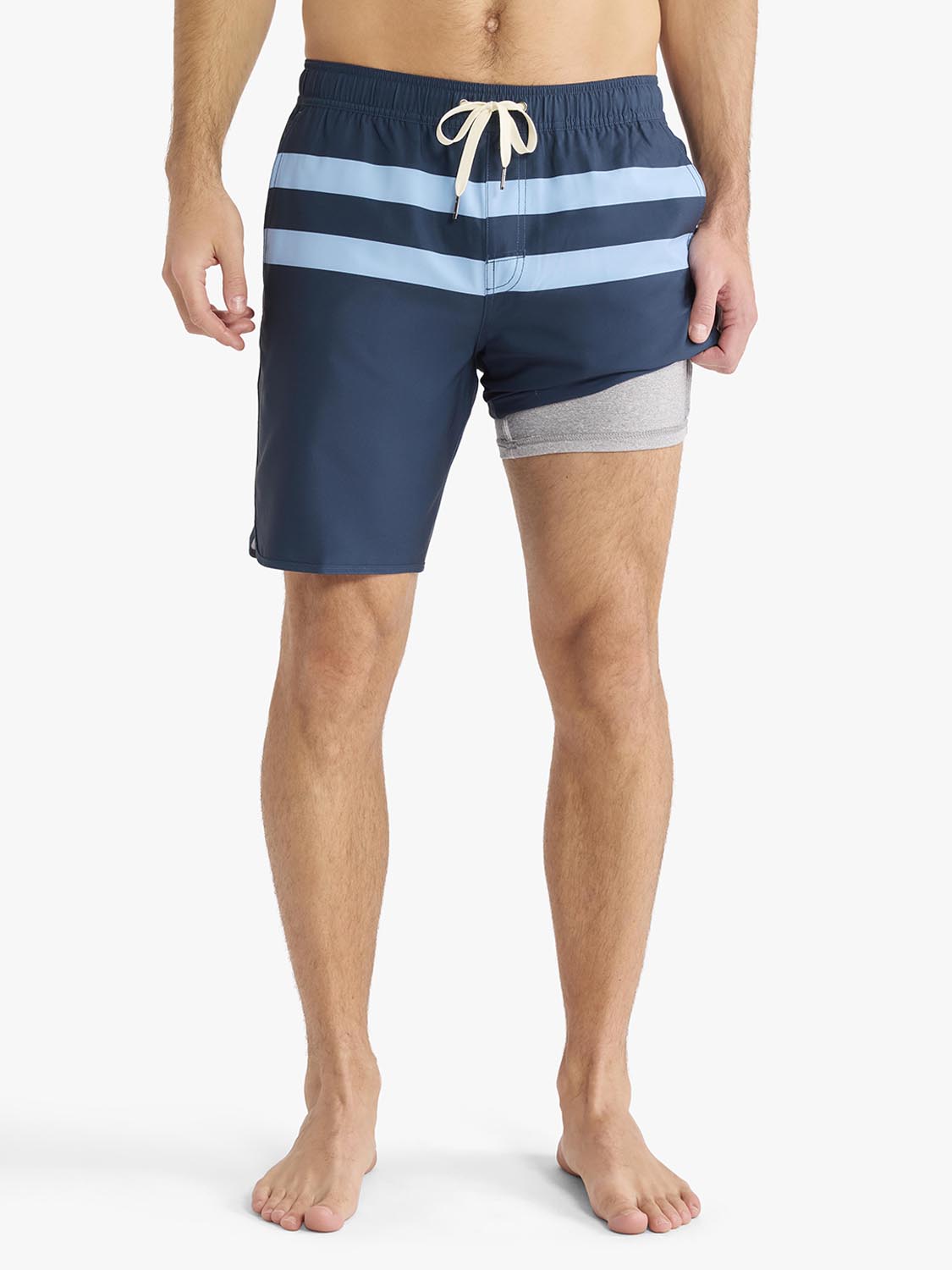 Man wearing navy swim trunks with light blue horizontal stripes and gray panel on right leg.