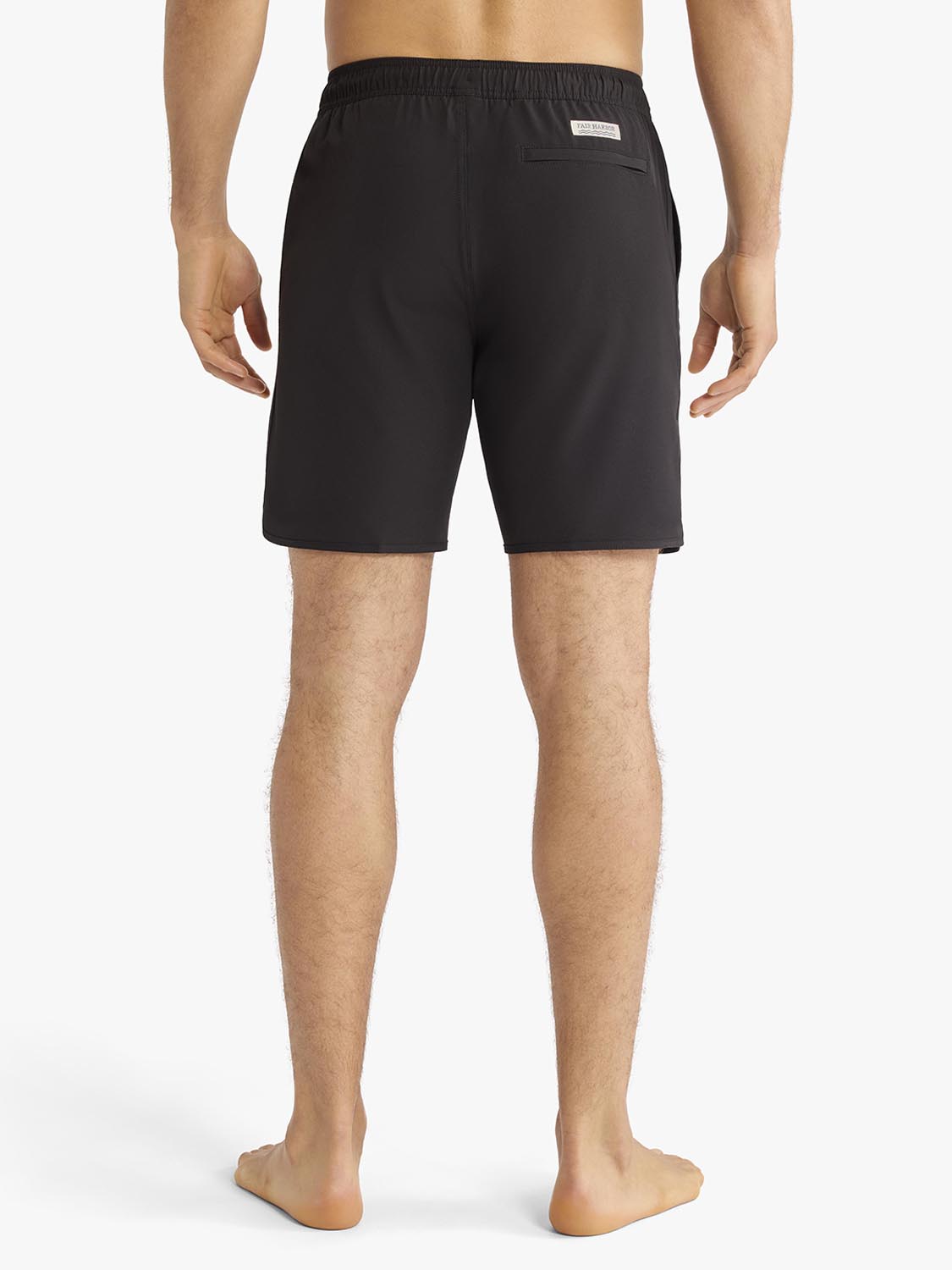 Man wearing black swim shorts with elastic waistband and rear pocket viewed from behind.