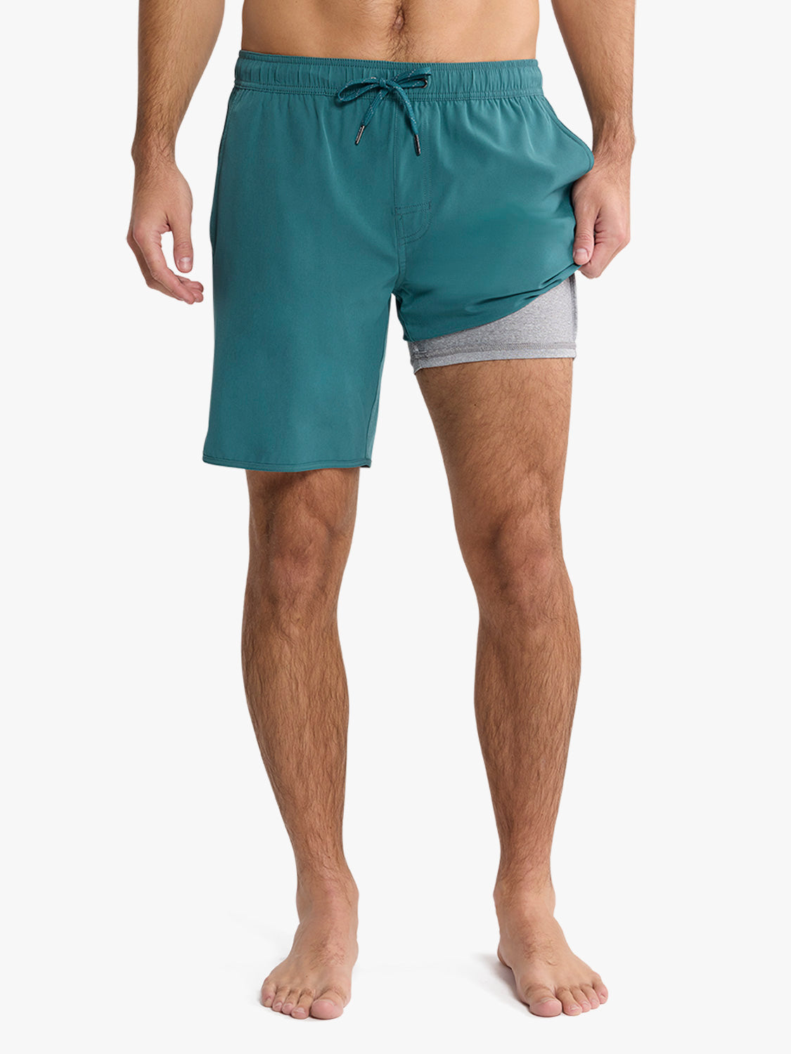 Man wearing seapine green swim trunks with gray mesh lining and drawstring closure.