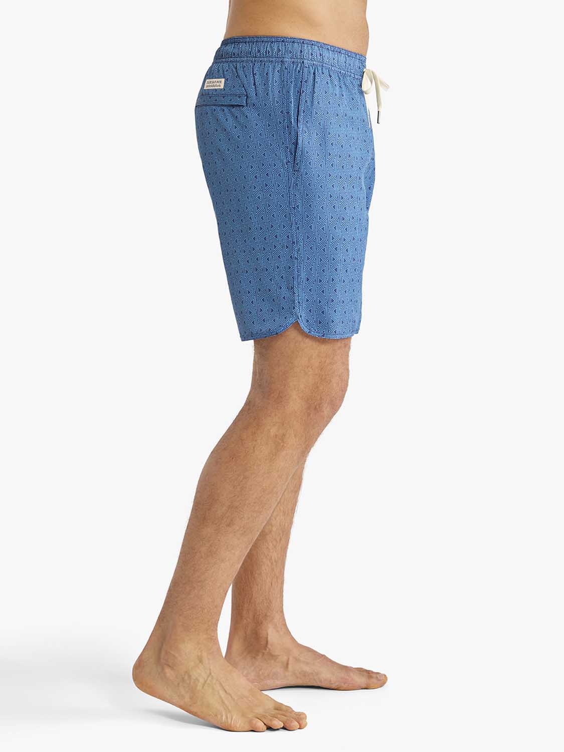 Man wearing electric blue geometric patterned swim trunks with drawstring and side pocket detail.