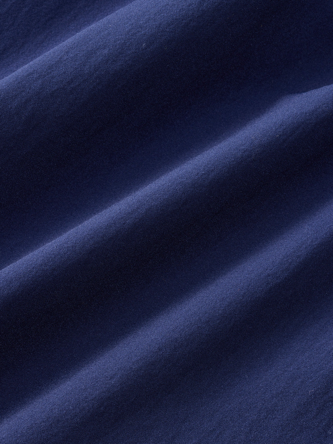 Navy blue fabric with diagonal folds and ribbed texture creating subtle shadow patterns.
