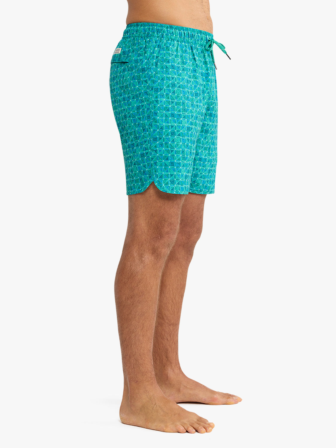 Man wearing turquoise swim trunks with geometric tile pattern and drawstring waistband.