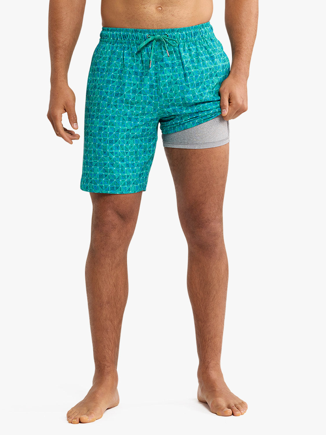 Man wearing turquoise swim shorts with geometric tile pattern and gray undergarment lining.