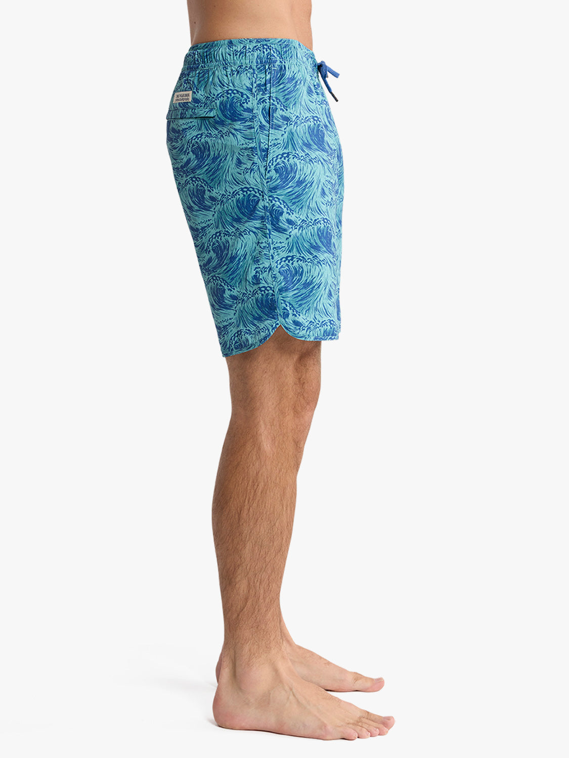 Man wearing blue wave-patterned swim trunks with drawstring waist and scalloped hem.