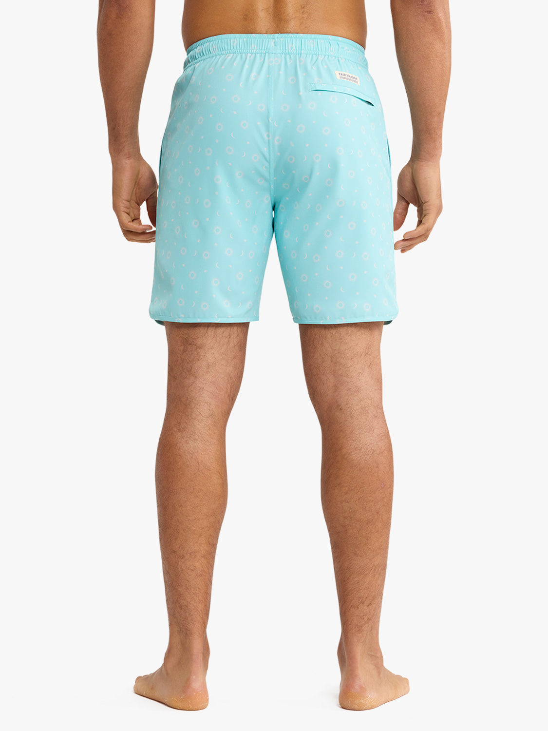 Man wearing turquoise swim trunks with small circular and star patterns throughout the fabric.