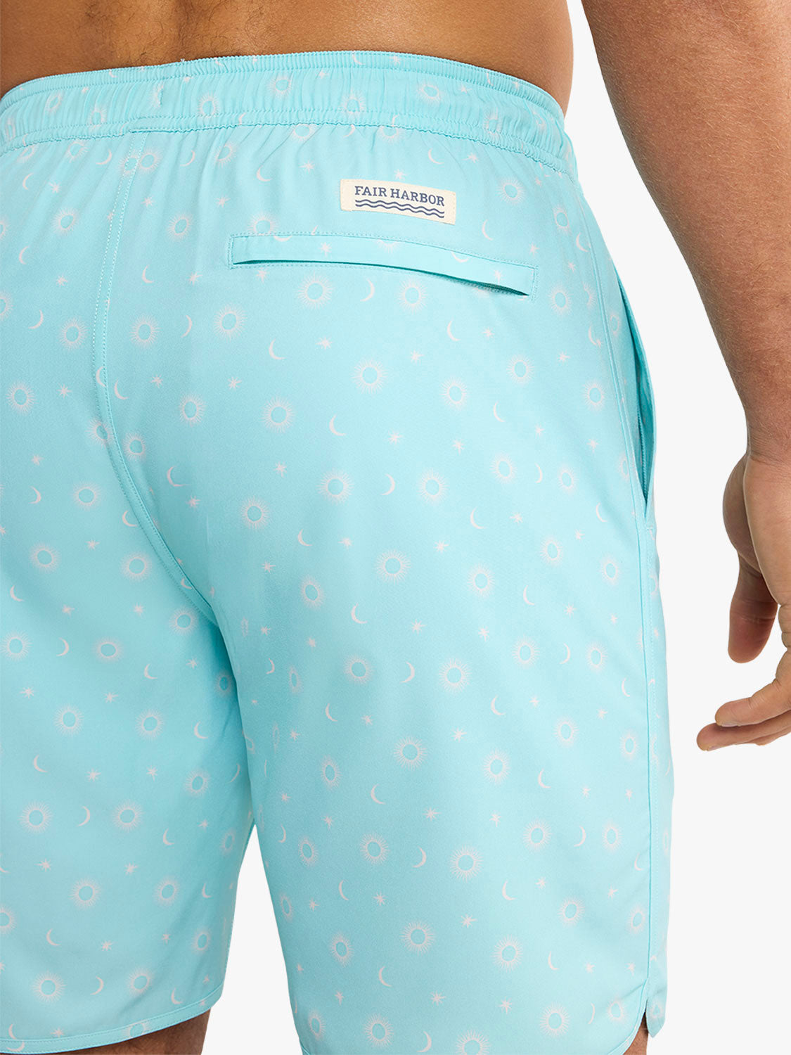 Turquoise swim trunks with white sun and moon star pattern and Fair Harbor brand label visible.