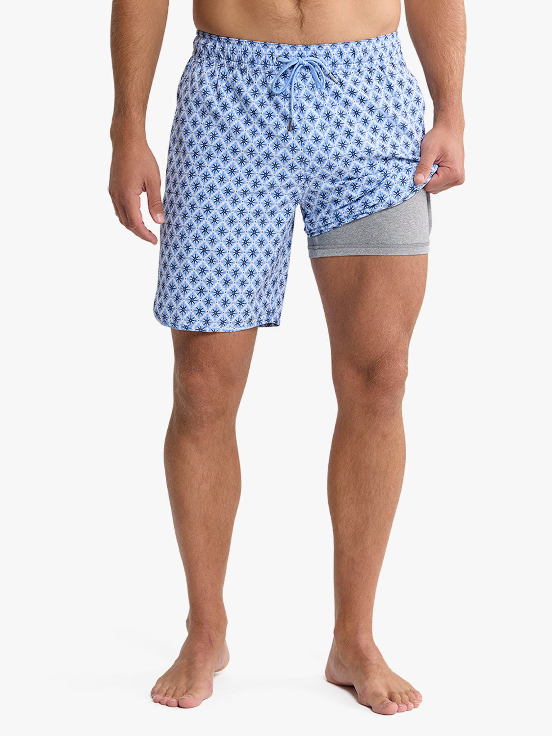 Man wearing blue swim trunks with star mosaic pattern and gray liner shorts underneath.