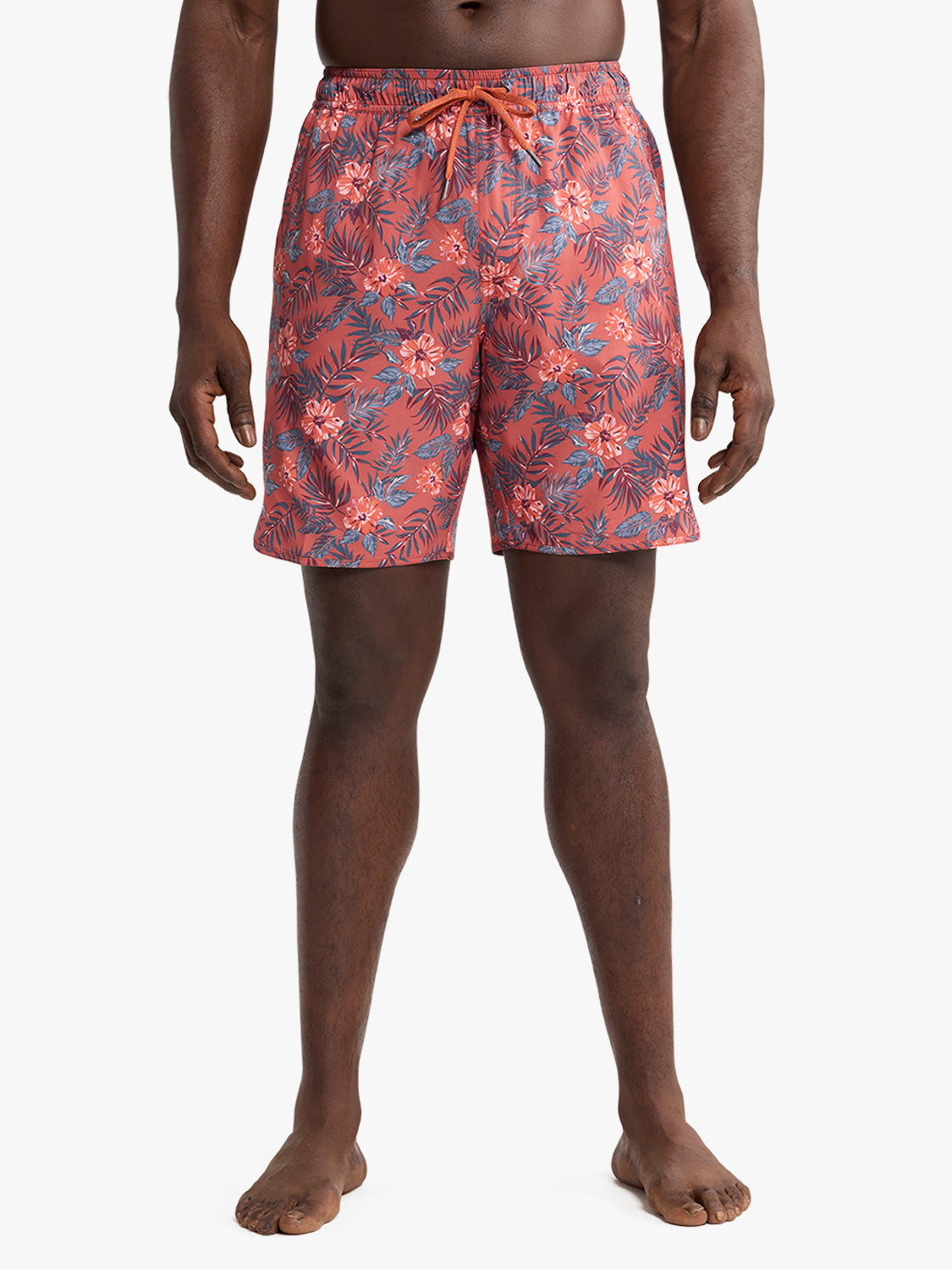 Red swim trunks with blue and coral tropical leaf and flower print pattern displayed on a man.