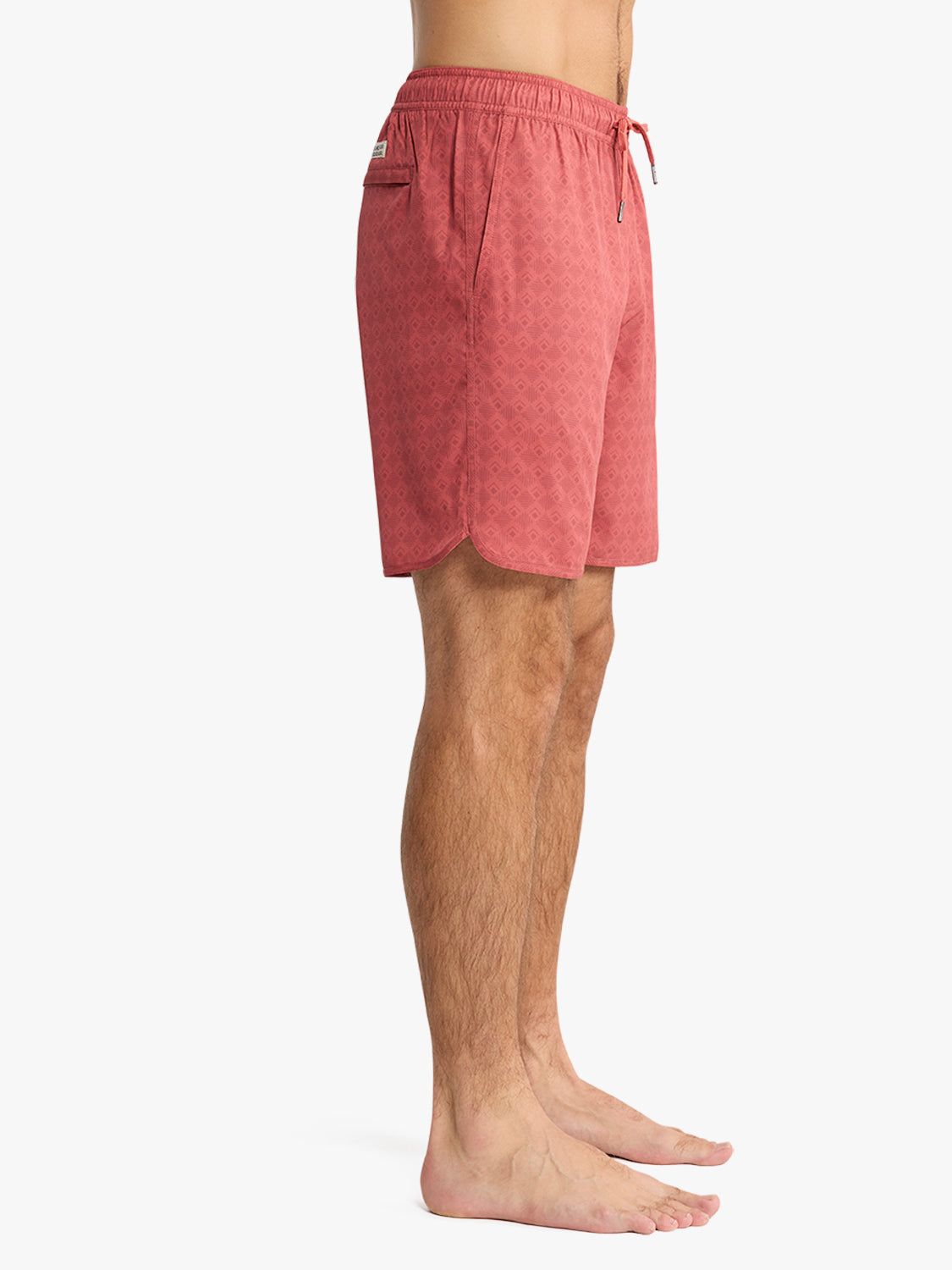 Man wearing red tile-patterned swim trunks with drawstring waist and side pockets.