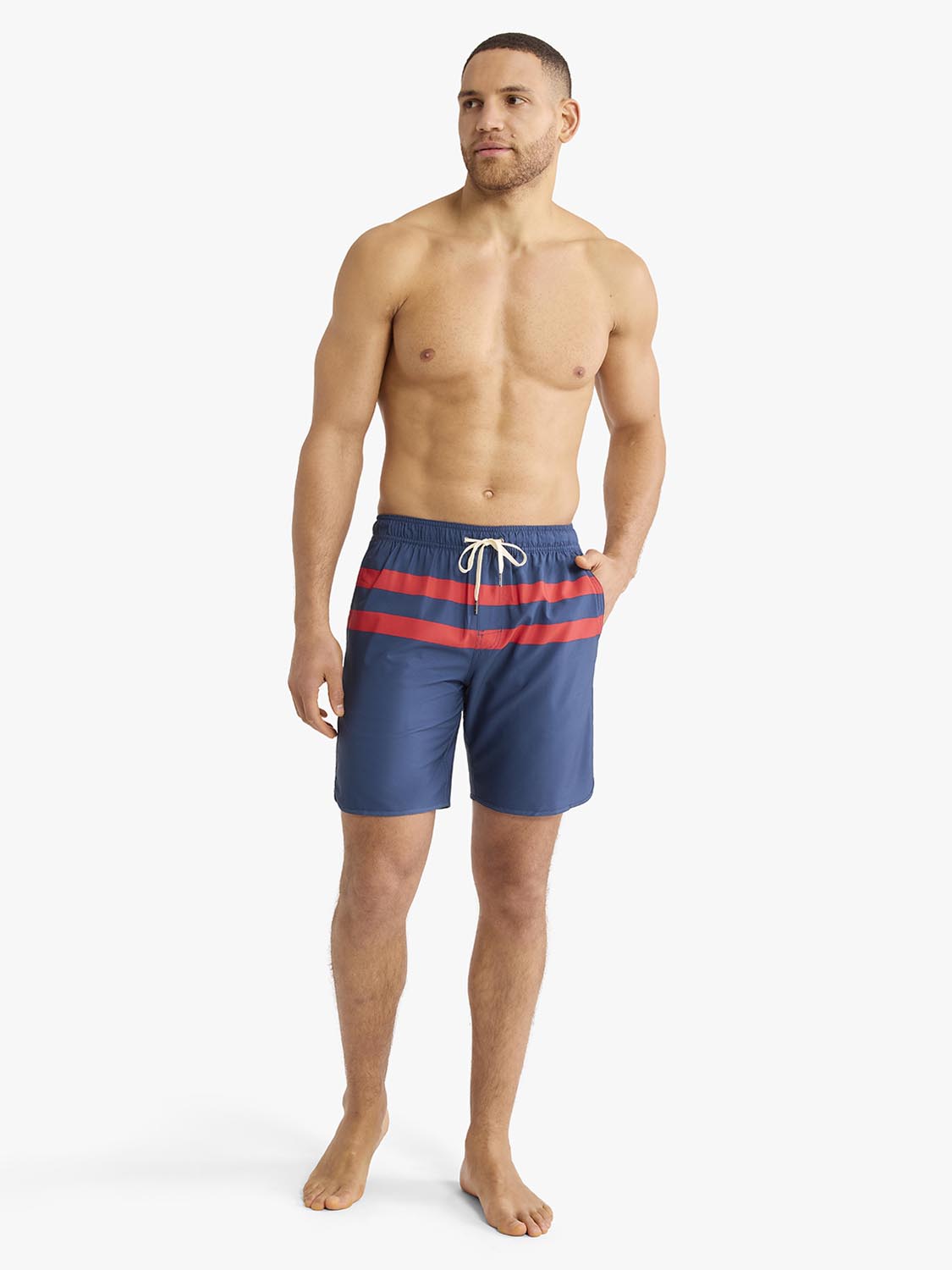 Man wearing navy swim trunks with red horizontal stripes and a drawstring waist.
