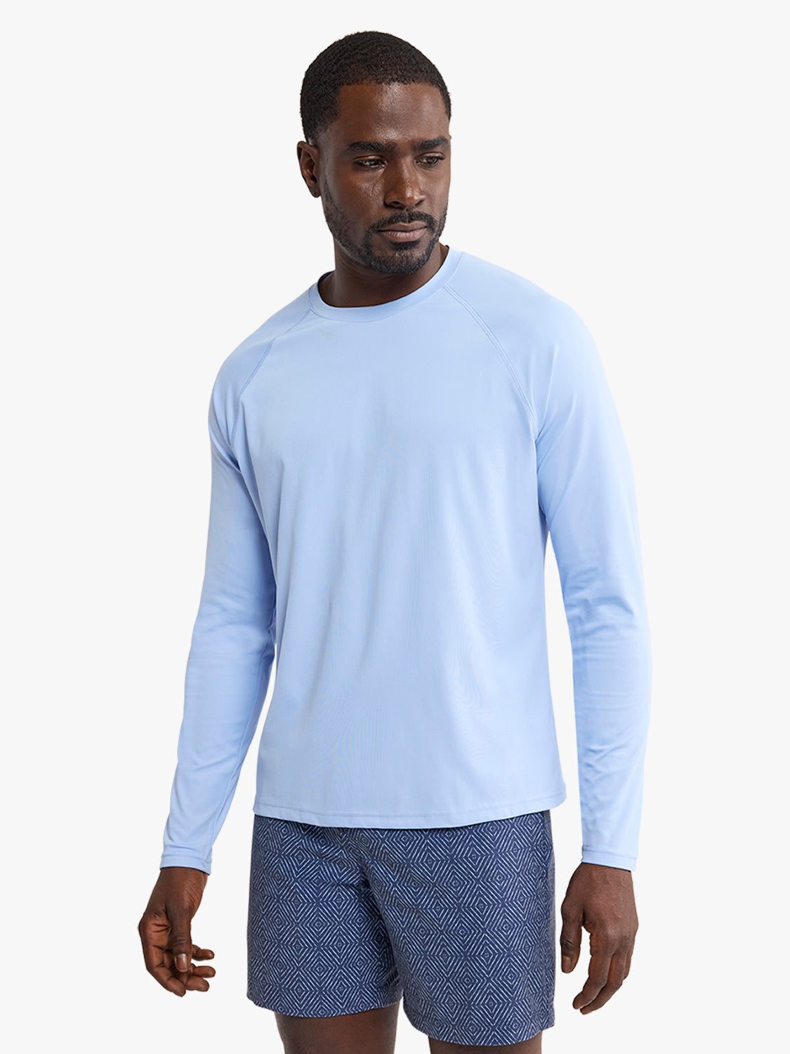 Man wearing a light blue long-sleeve rashguard with patterned swim shorts.