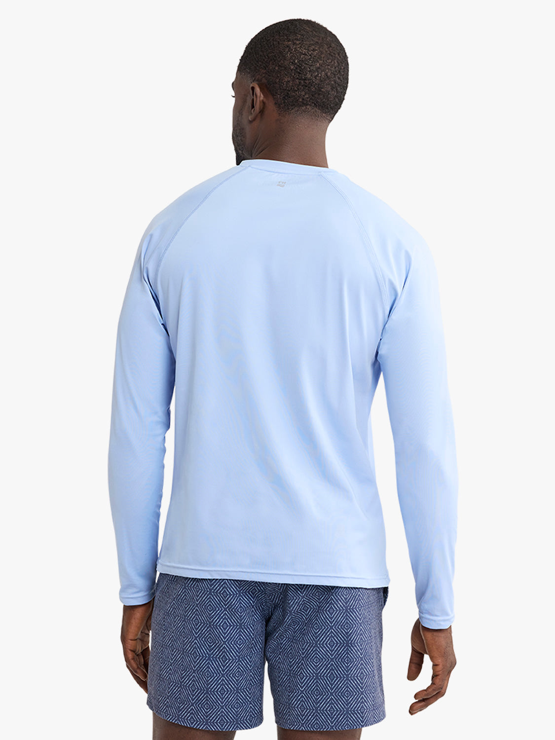 Man wearing light blue long-sleeved rashguard viewed from the back against white background.
