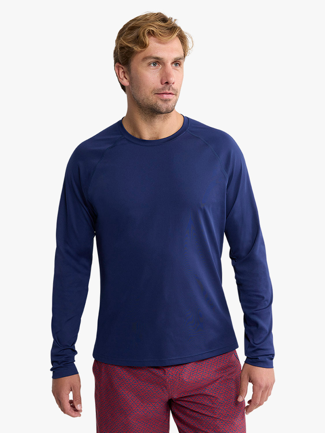 Man wearing a navy long-sleeved rashguard with a crew neckline and burgundy patterned swim shorts.