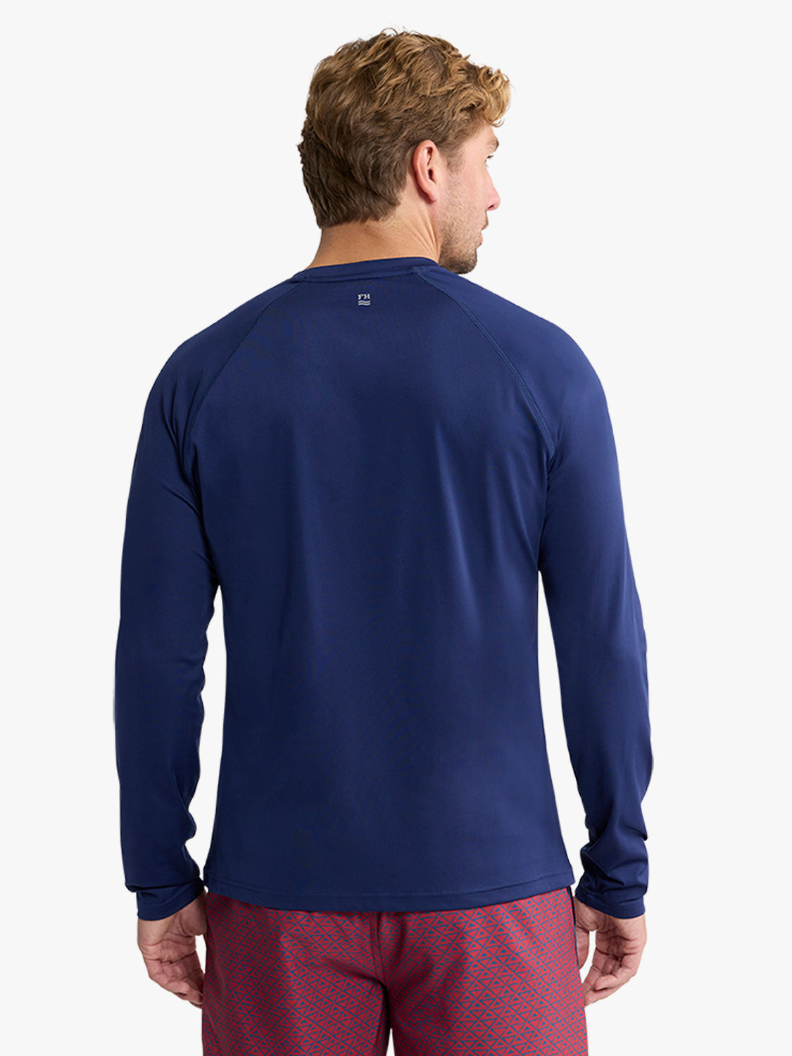 Man wearing a navy long-sleeved rashguard with burgundy patterned swim shorts, shown from behind.