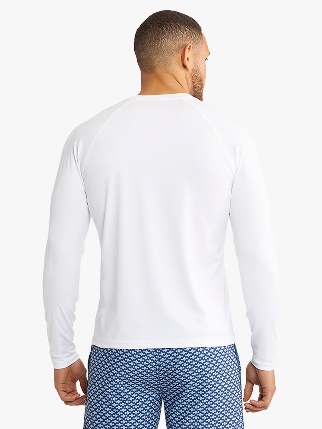 Man wearing a white long-sleeved rashguard with blue patterned swim shorts, shown from behind.