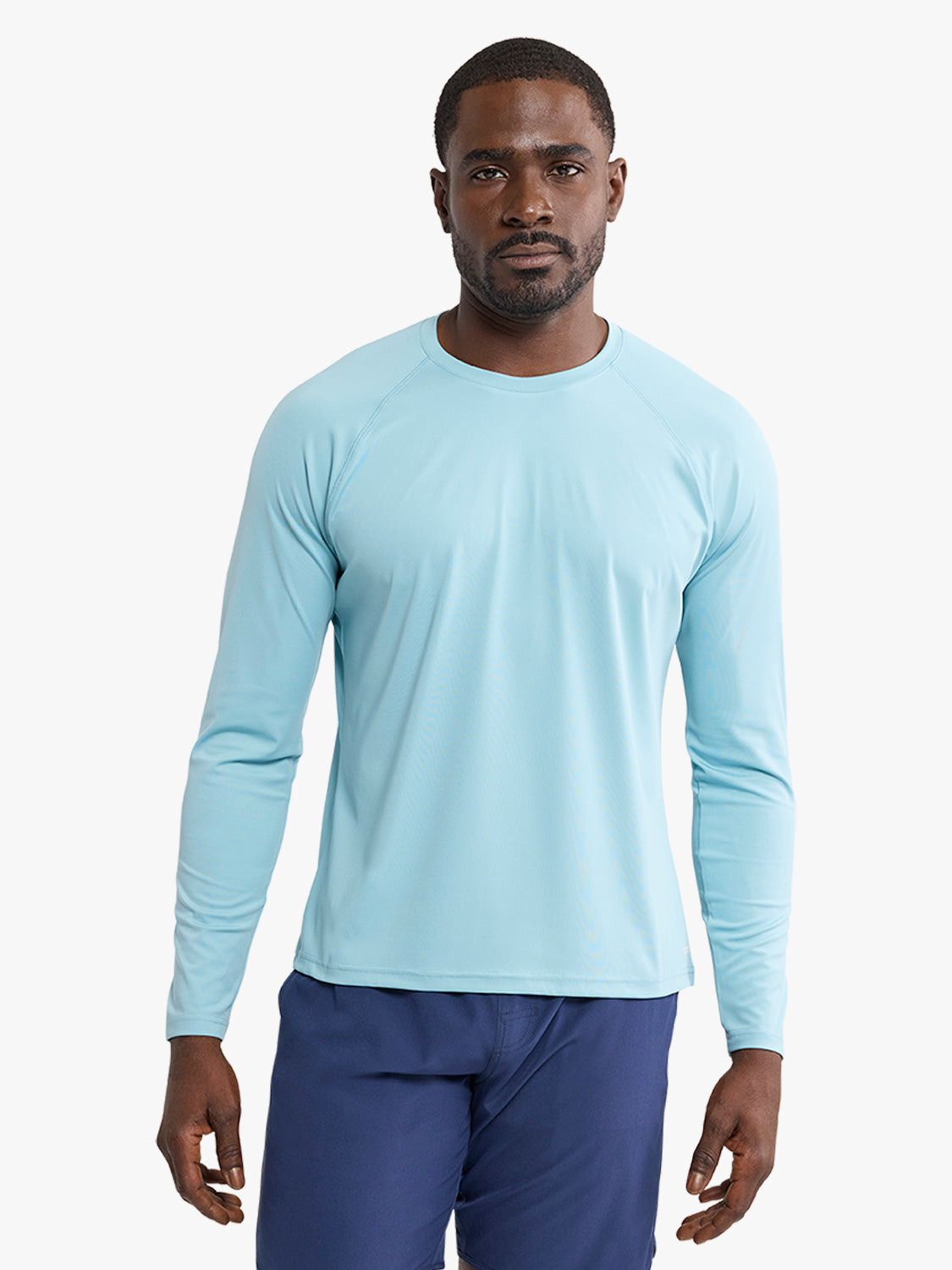 Man wearing a light blue long-sleeve rashguard with navy swim shorts against a white background.