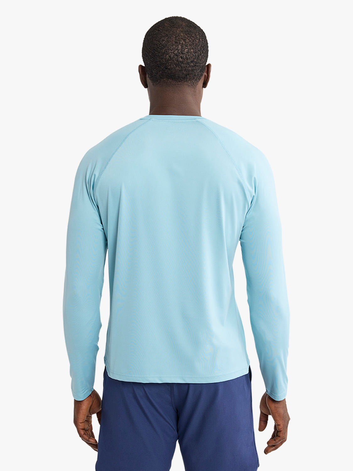 Man wearing a light blue long-sleeved rashguard with navy shorts, shown from behind.