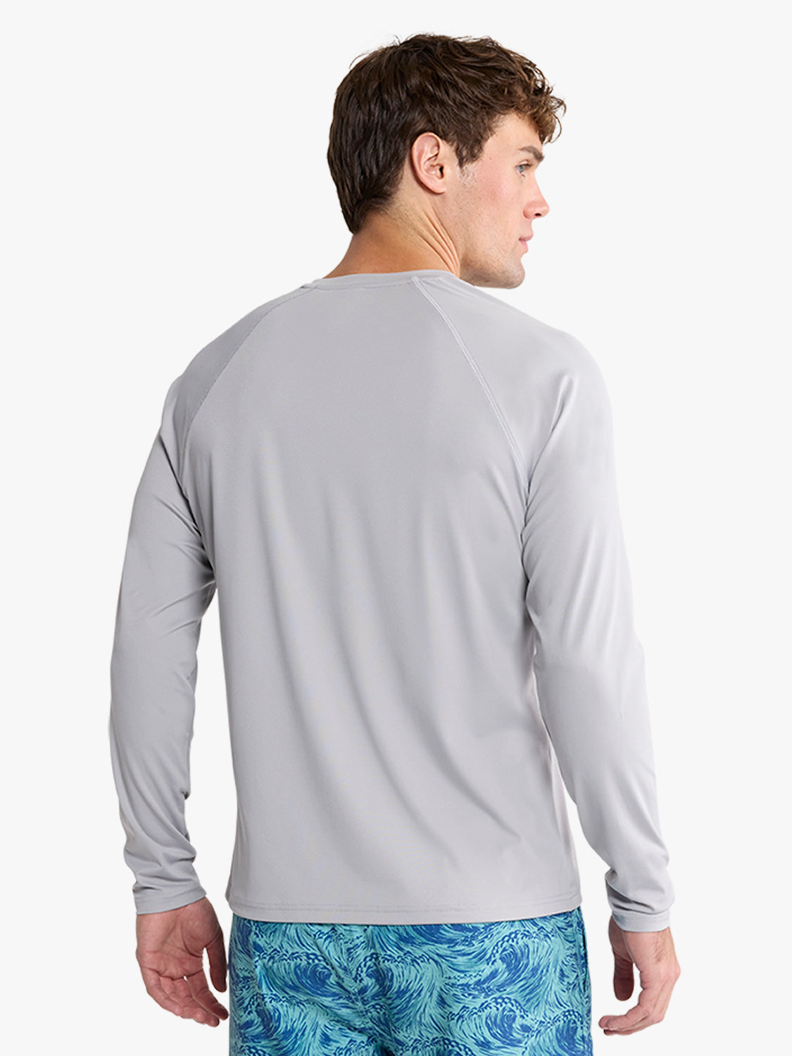 Man wearing light gray long-sleeve rashguard viewed from behind against white background.