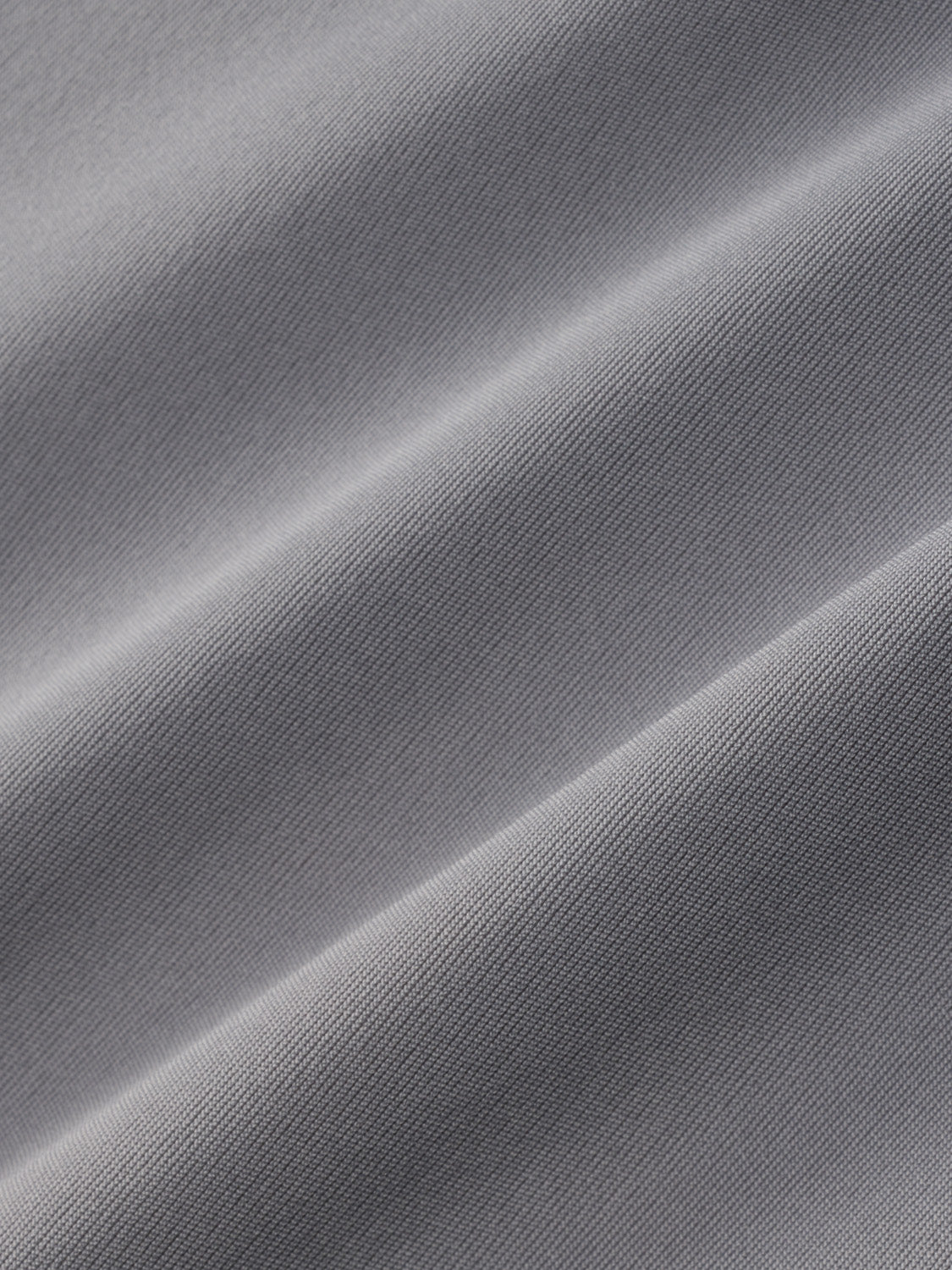 Gray rashguard fabric with textured weave and diagonal folds creating subtle shadows.