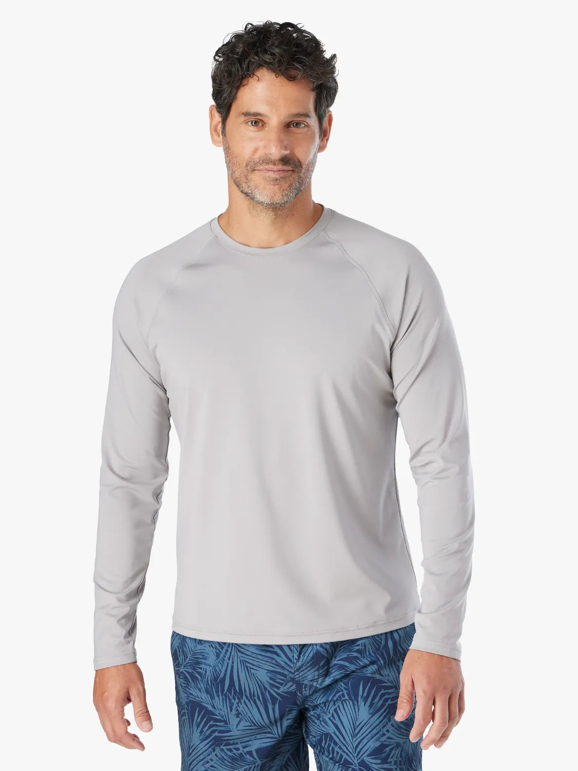 Man wearing a grey long-sleeved rashguard with a crew neckline and blue patterned swim shorts.