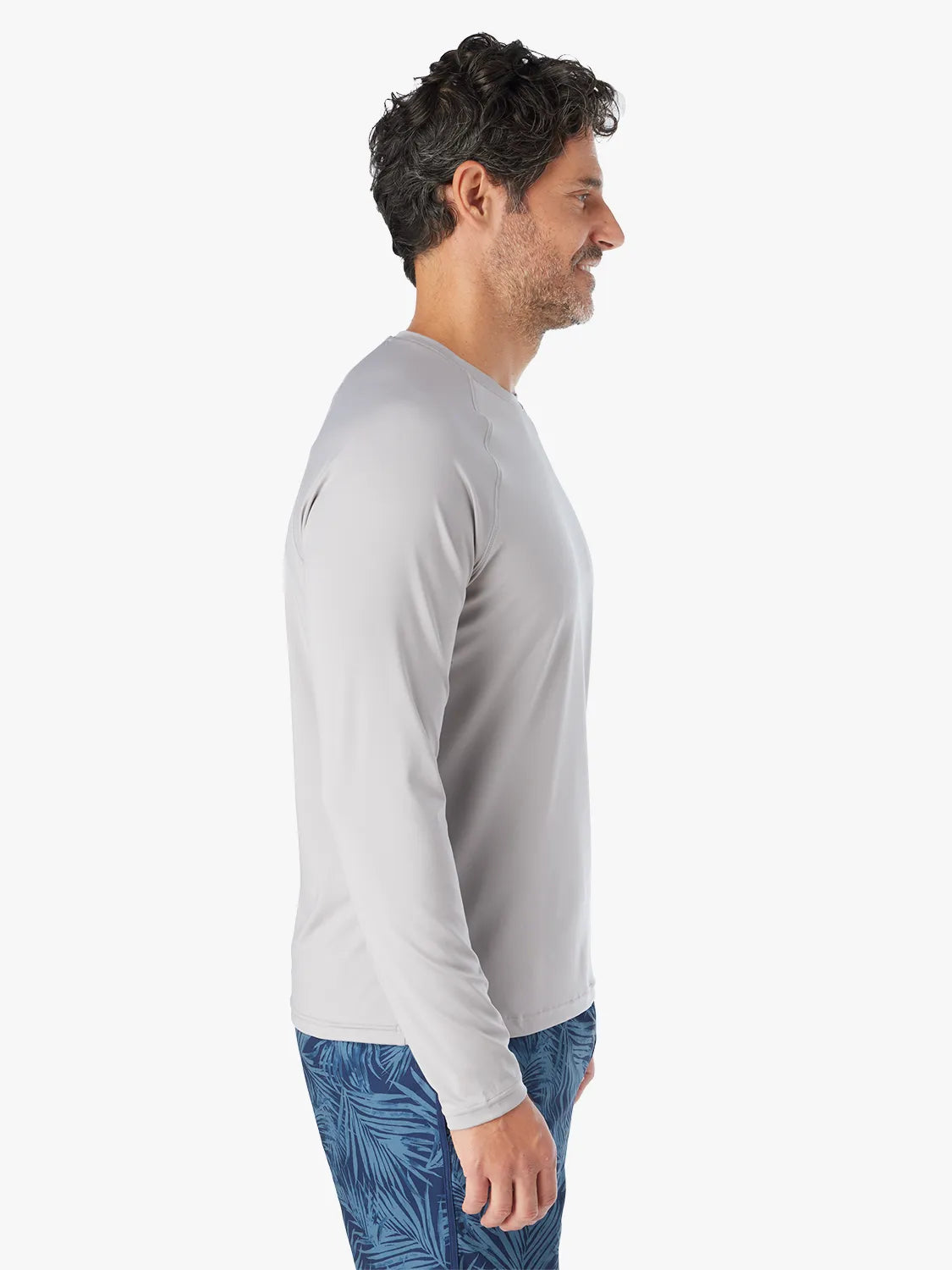 Man wearing a grey long-sleeved rashguard with blue patterned swim trunks, shown in profile view.