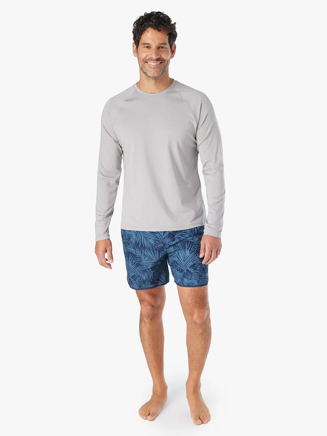 Man wearing a grey long-sleeve rashguard with blue patterned swim shorts.