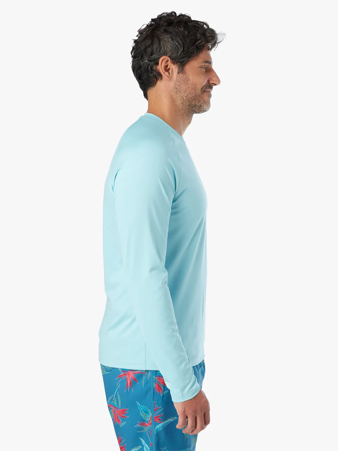 Man wearing an aqua long-sleeve rashguard with floral swim trunks, shown in side profile.