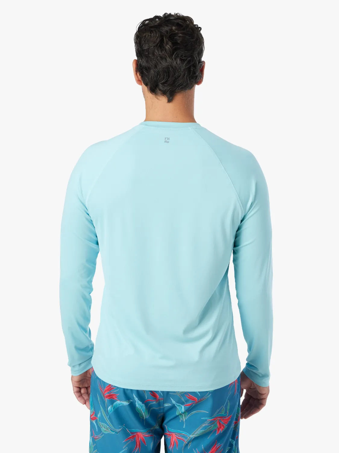Man wearing light aqua long-sleeved rashguard viewed from the back against white background.