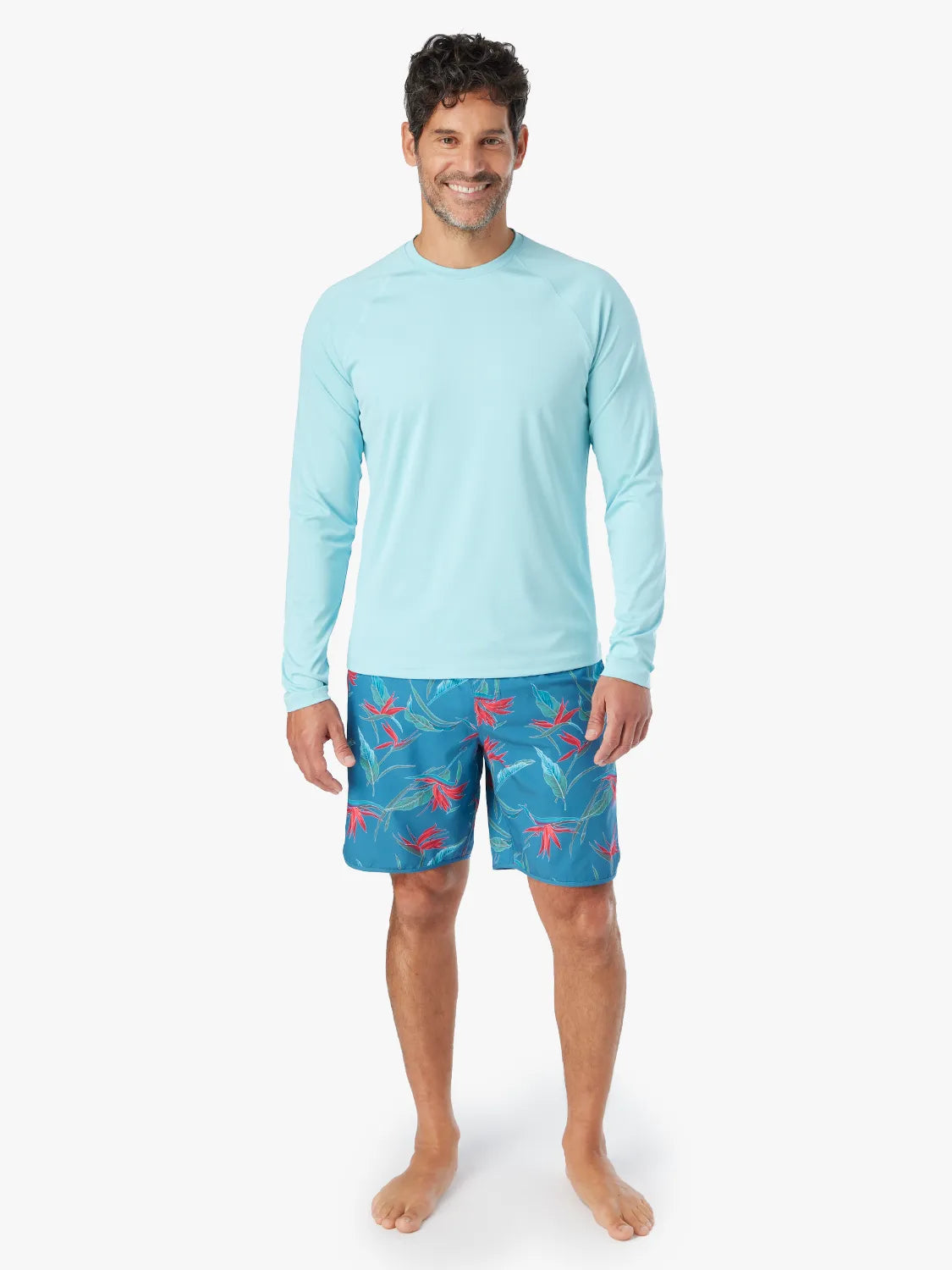 Man wearing an aqua long-sleeve rashguard with blue patterned swim shorts.