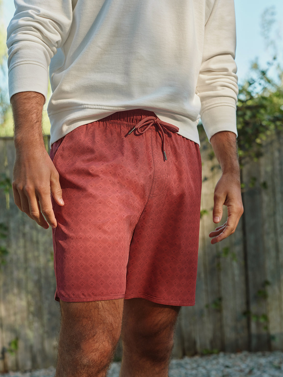 Man wearing cream-colored sweatshirt and red tile-patterned shorts with drawstring waistband outdoors.