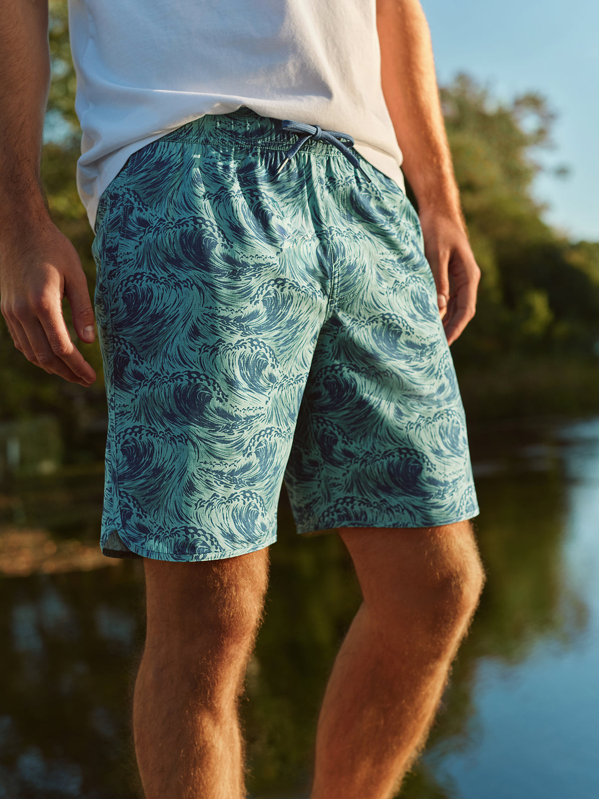 Man wearing teal and navy patterned swim shorts with star mosaic design near water.