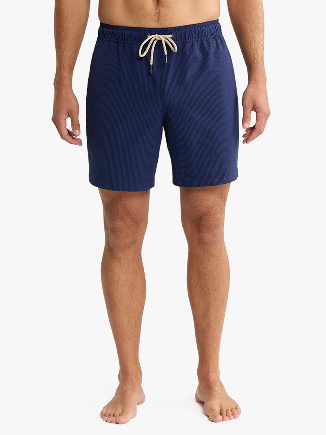 Man wearing navy seersucker swim trunks with cream drawstring waistband and textured fabric.