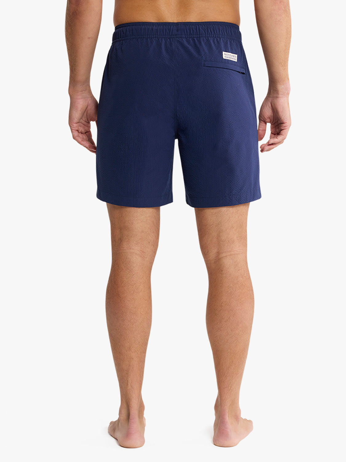 Man wearing navy seersucker swim trunks with elastic waistband viewed from behind.