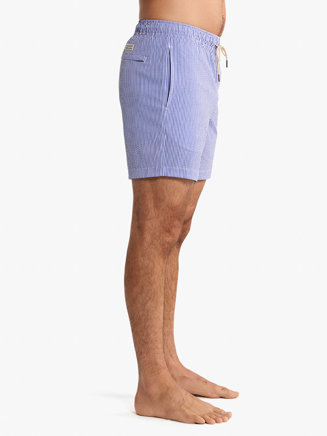 Man wearing light blue seersucker swim trunks with vertical stripe pattern and drawstring waist.
