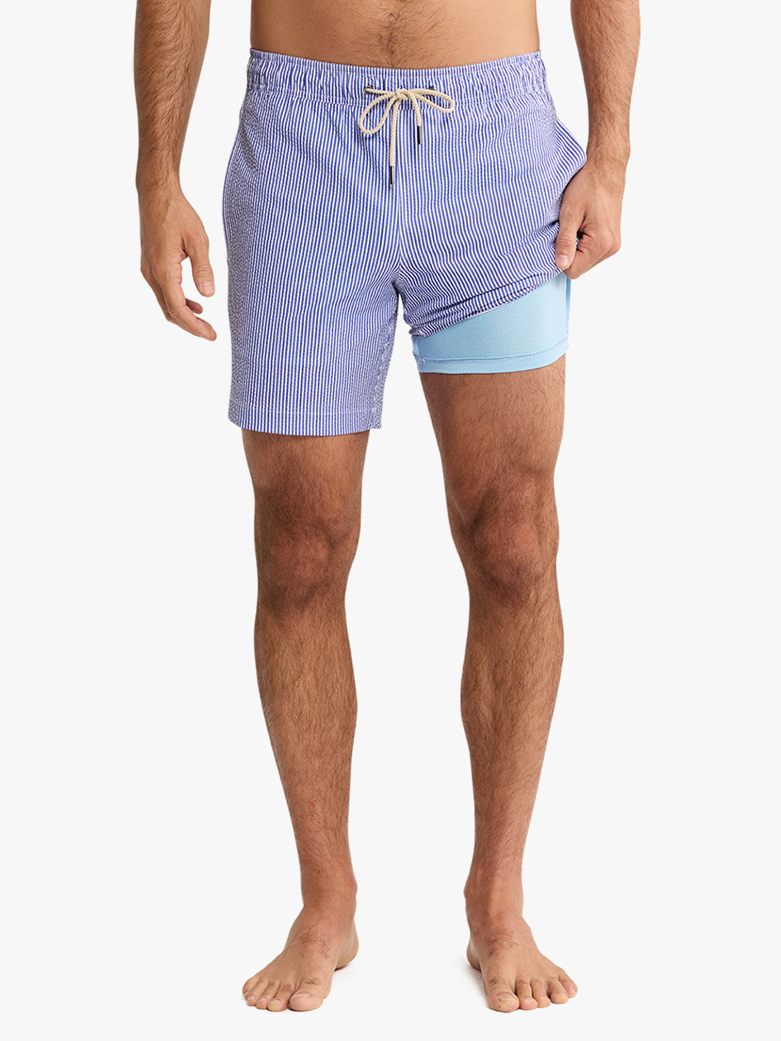 Man wearing blue and white striped seersucker swim trunks with light blue inner shorts and drawstring.