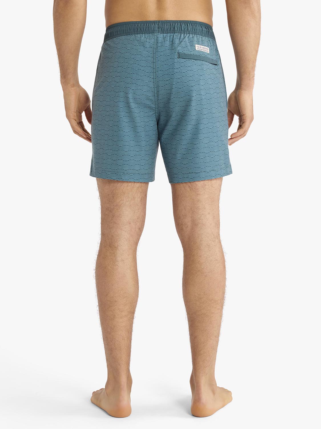 Man wearing teal swim trunks with horizontal wave pattern, shown from behind.