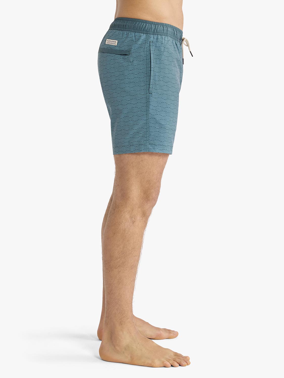 Man wearing teal green wave-patterned swim trunks with drawstring waistband and side pocket.