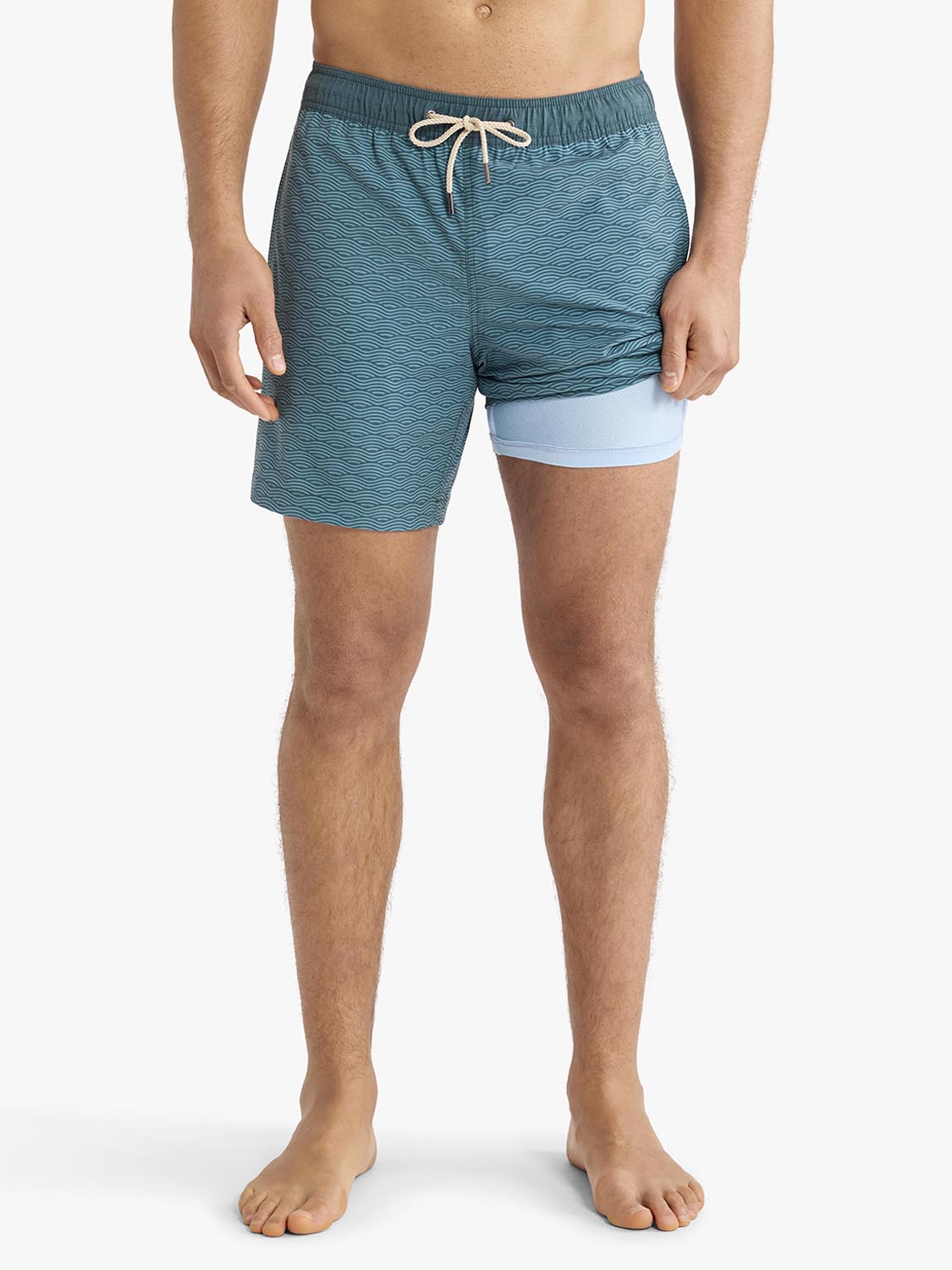 Man wearing teal textured swim trunks with light blue contrast liner and white drawstring.