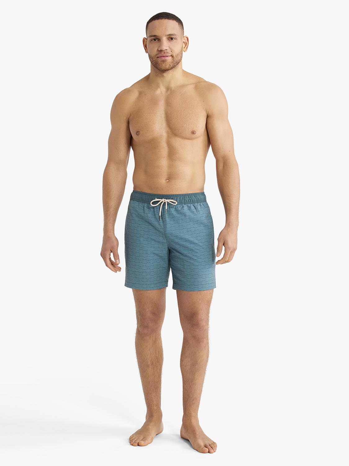 Man wearing teal green swim trunks with a textured wave pattern and drawstring waistband.