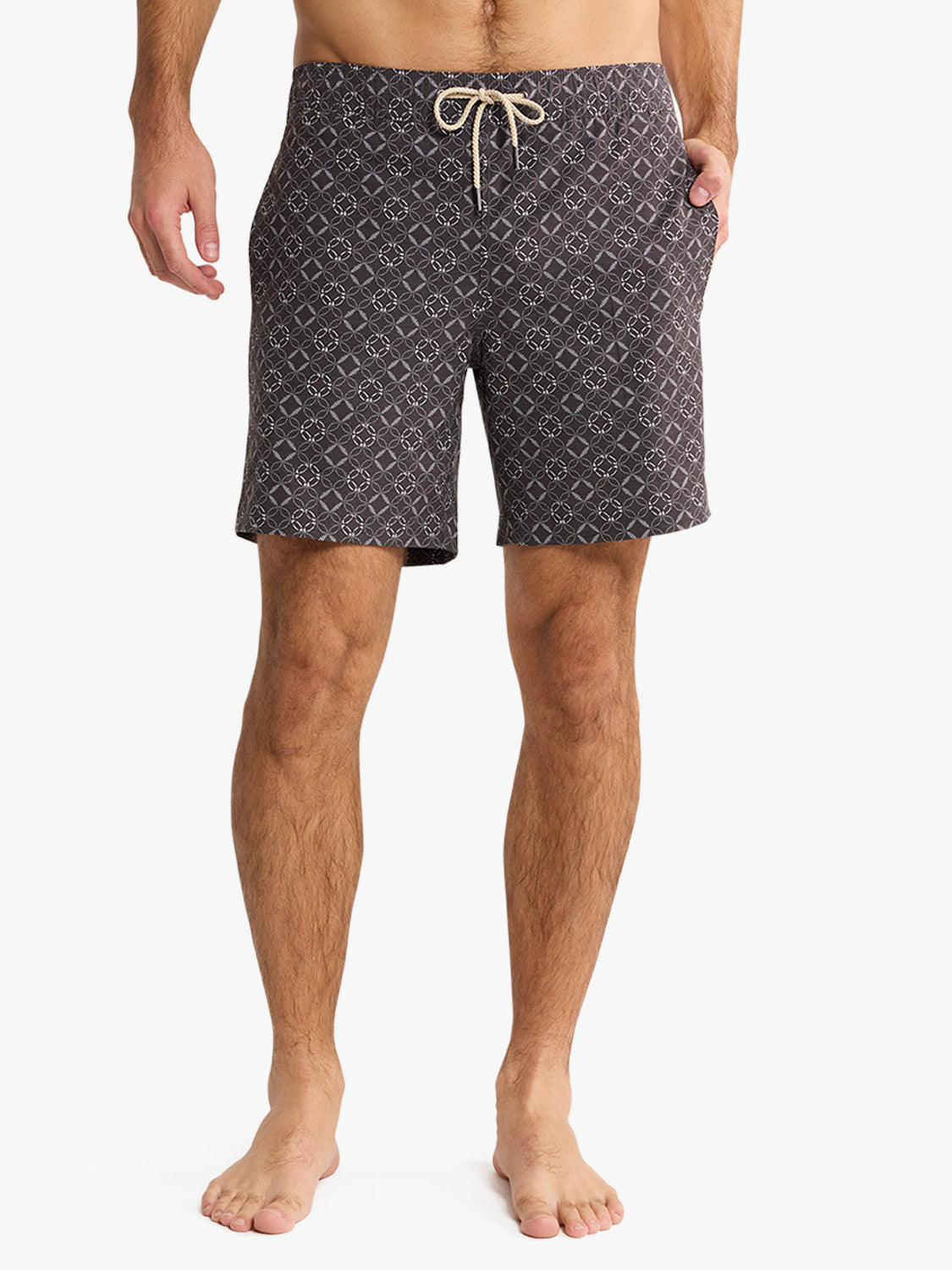 Man wearing charcoal swim trunks with white geometric circle pattern and drawstring waist.