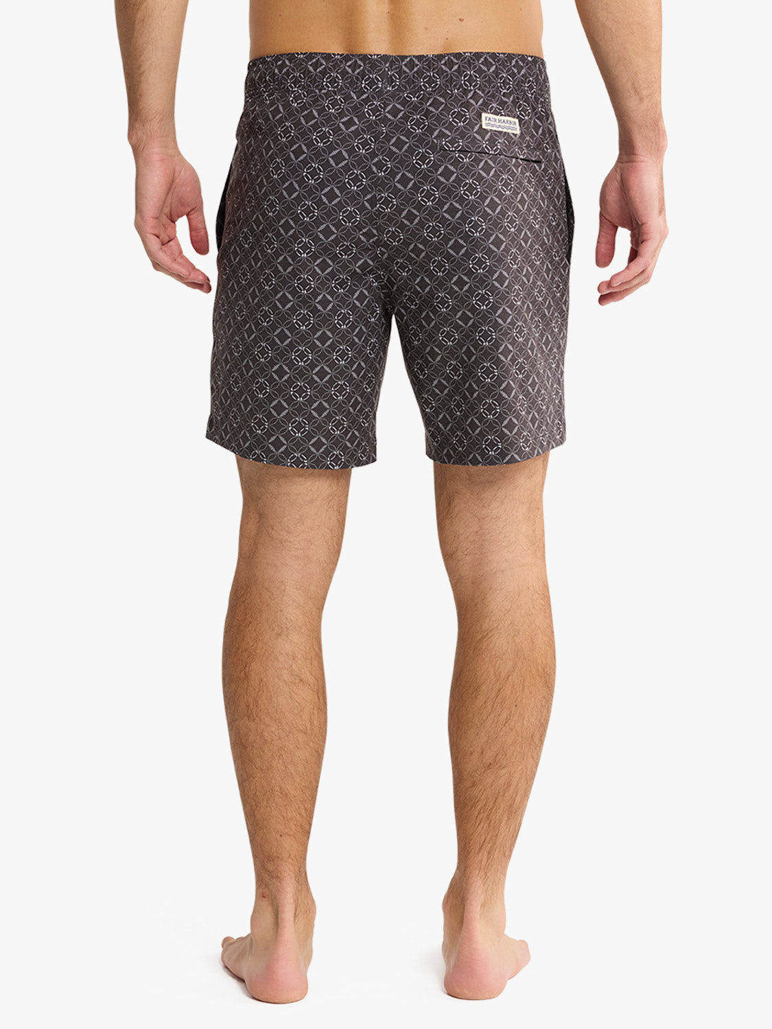 Man wearing dark gray swim trunks with geometric circle pattern and white brand label.