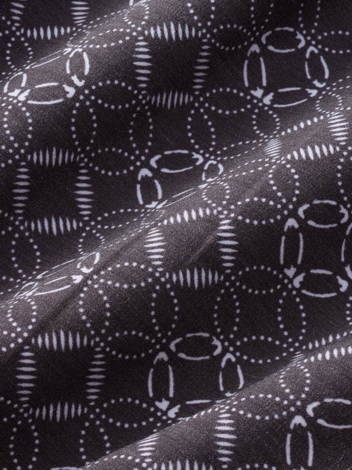 Dark fabric with white geometric circles, dotted lines, and striped patterns repeating across the surface.