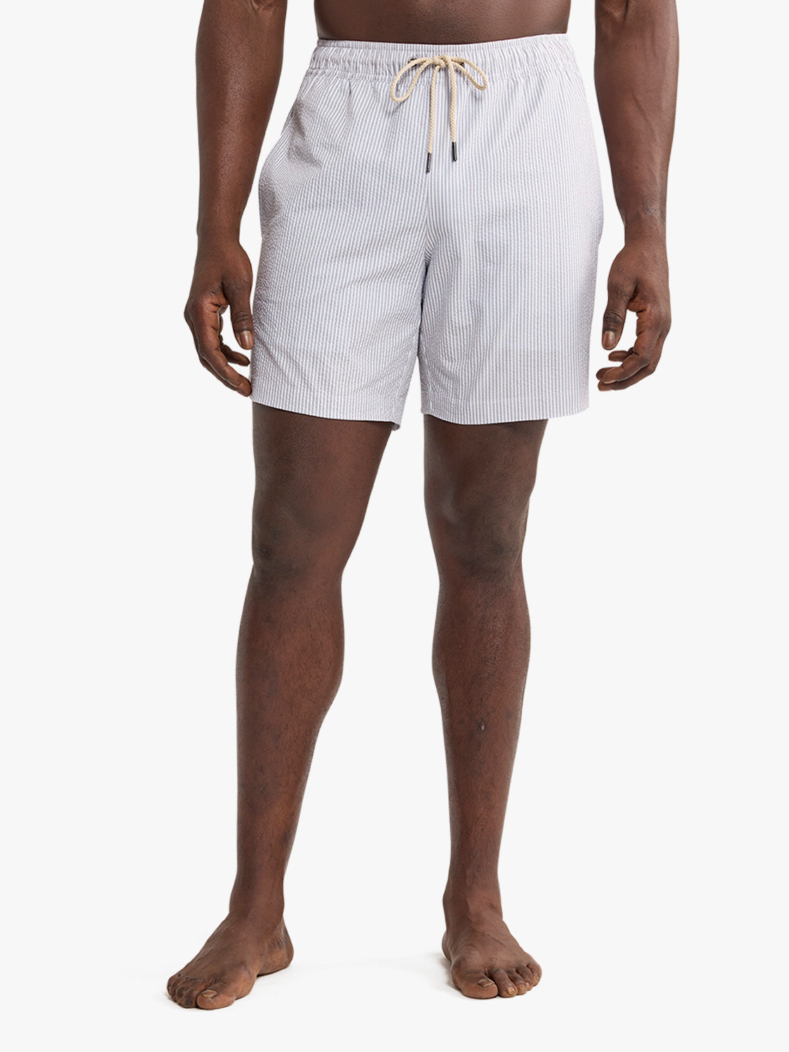Man wearing grey seersucker swim trunks with vertical stripe pattern and drawstring waist.
