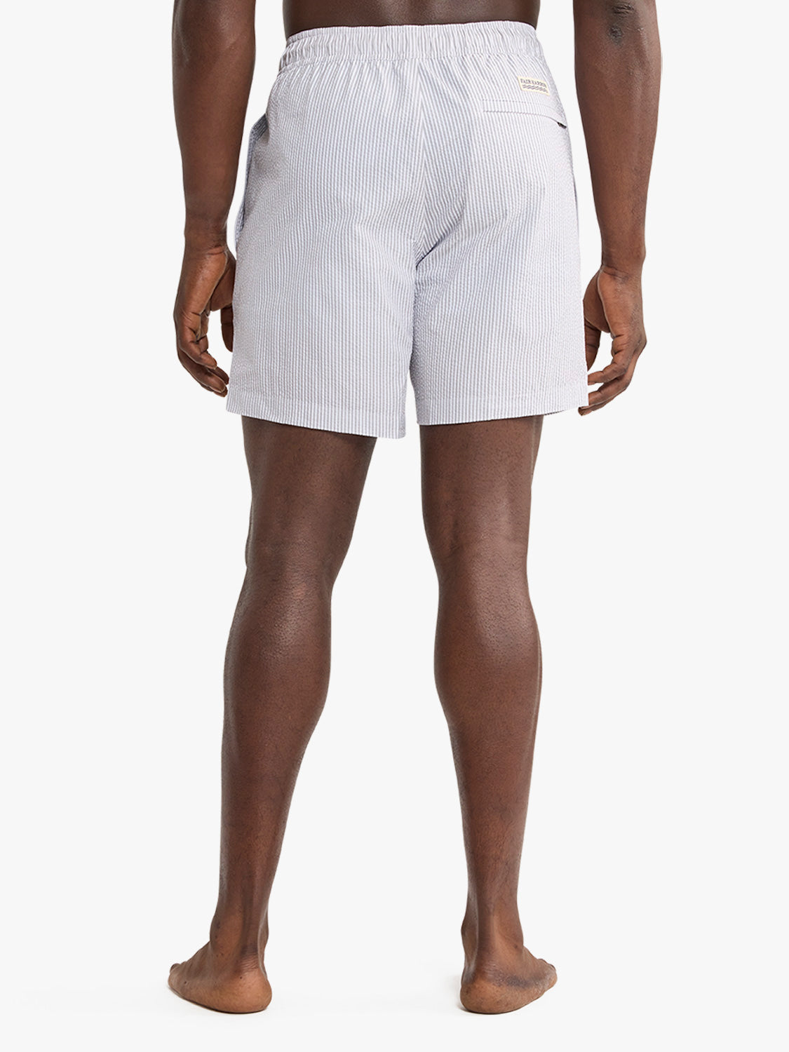 Man wearing light grey seersucker swim trunk with vertical stripe pattern shown from behind.