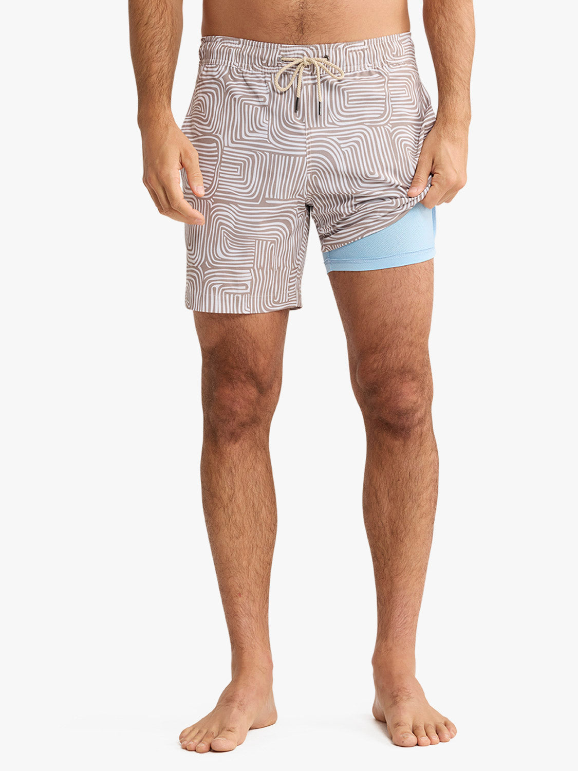 Man wearing tan and white wavy patterned swim trunks with blue compression shorts underneath.
