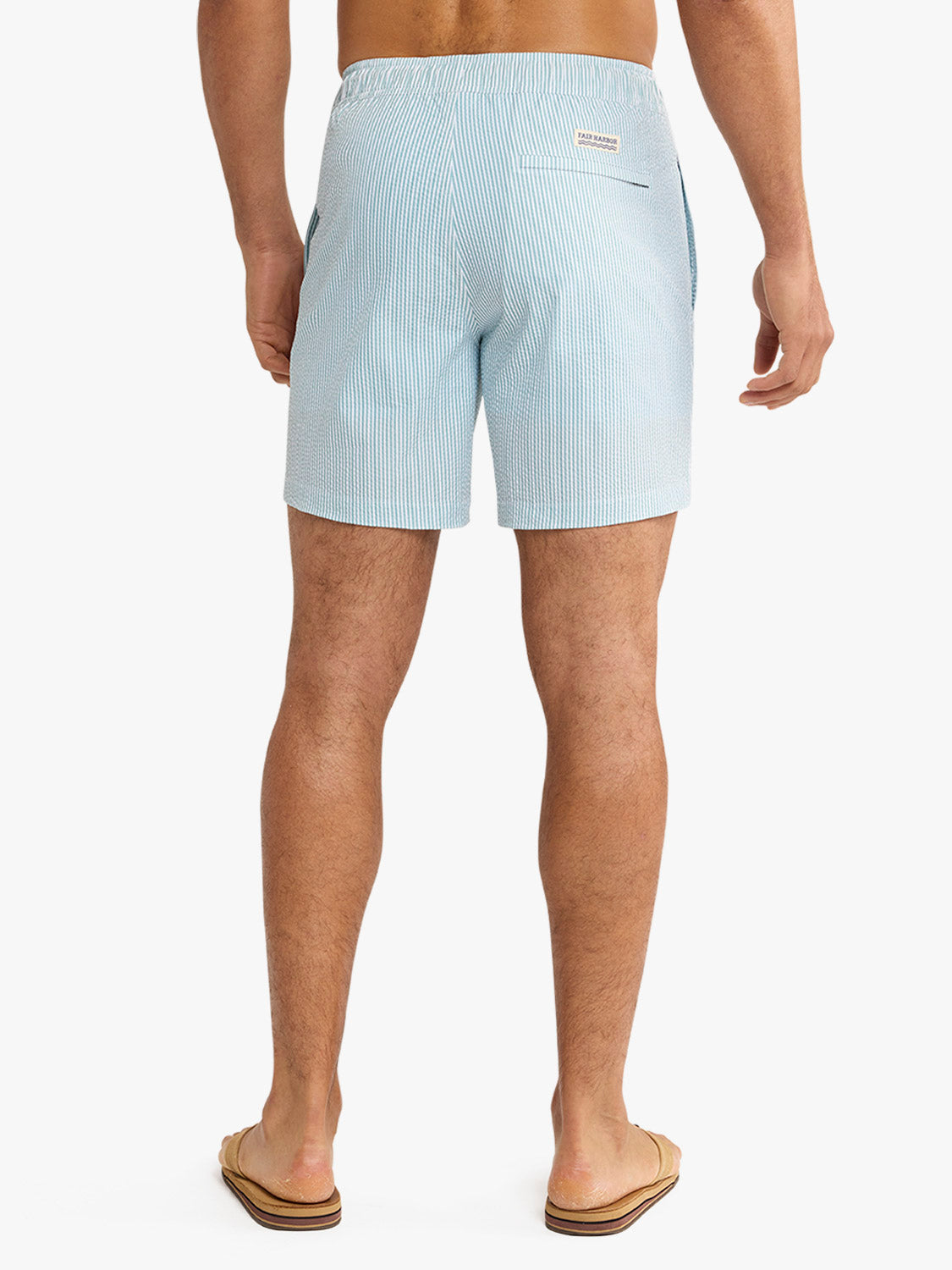 Man wearing light blue seersucker swim trunk with vertical stripe pattern, shown from behind.