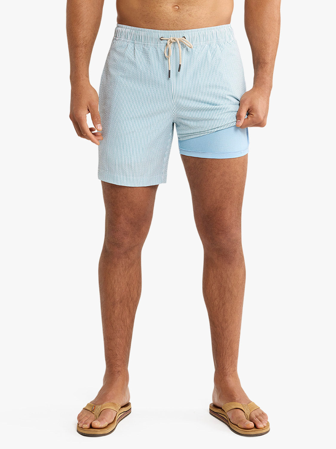 Man wearing light blue seersucker swim trunks with drawstring and built-in liner shorts.