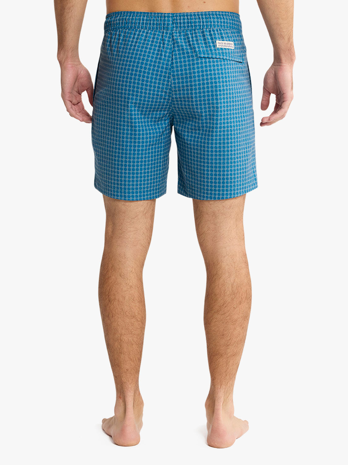 Man wearing teal swim trunks with a geometric grid pattern shown from behind.